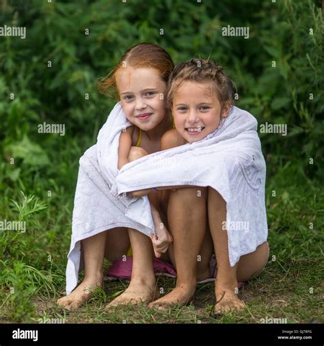 Two naughty little girls sitting on the beach in a towel after a bathe ...