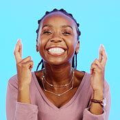 Face, fingers crossed and black woman with smile, hope and motivation with lady against blue ...