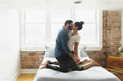 Romantic couple kissing while kneeling on bed at home - Stock Photo ...