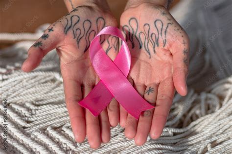 Manos de mujer con tatuajes sosteniendo listón rosa por el día contra ...