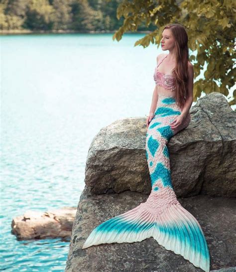 a woman sitting on top of a rock next to a body of water with a mermaid tail