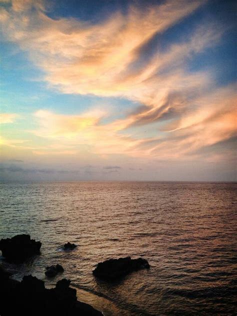 the sun is setting over the ocean with rocks in the foreground and clouds in the background