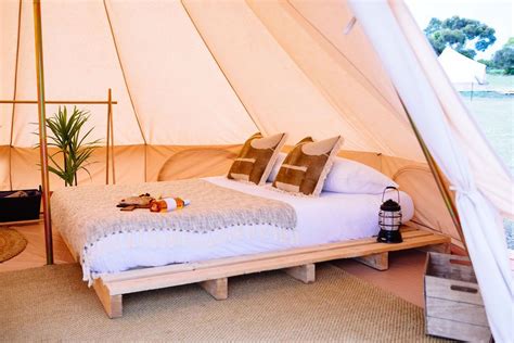 a bed sitting inside of a white tent next to a wooden table and lamp on top of it