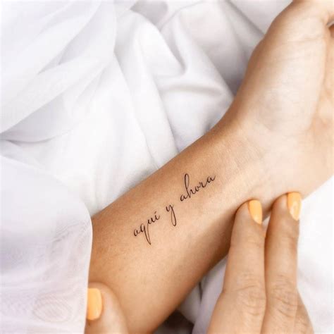 "Aqui y ahora" lettering tattoo on the wrist.