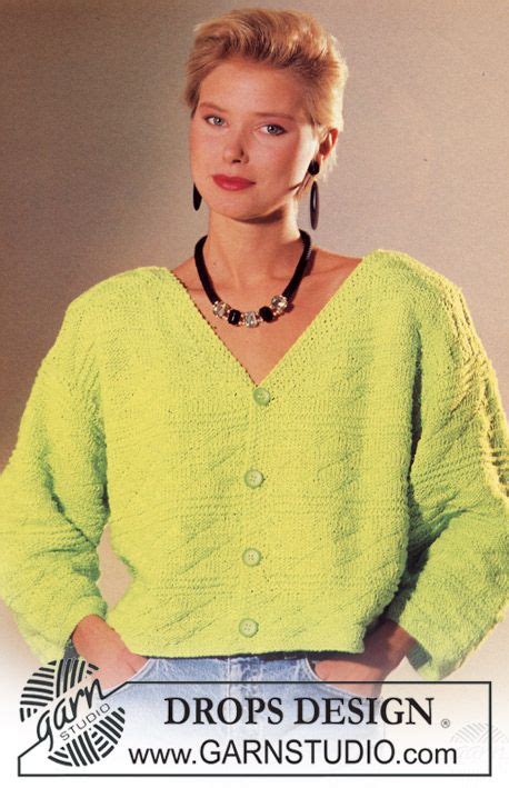 a woman wearing a yellow sweater and black necklace standing in front of a white wall