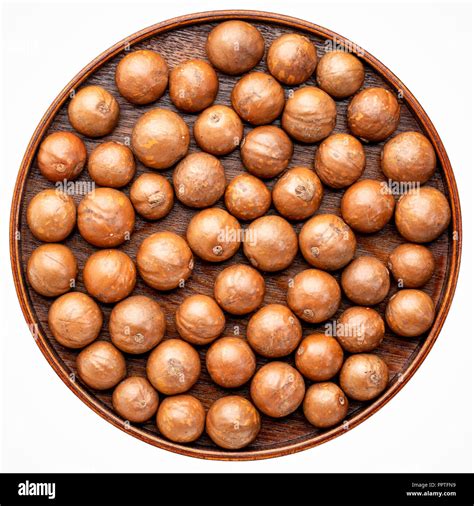 macadamia nuts in shells on on a round wooden tray isolated on white ...