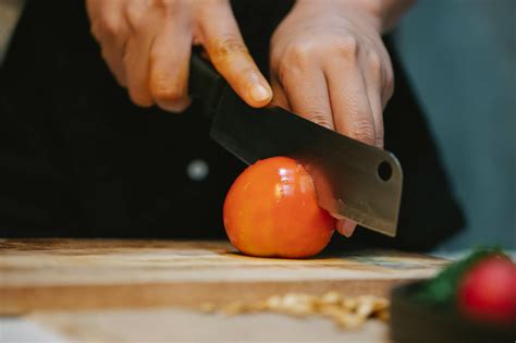 Chef cutting tomato with knife on wooden cutting board · Free Stock Photo
