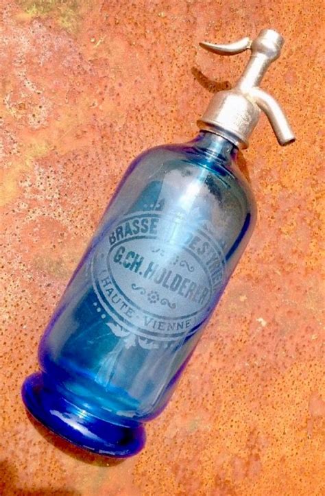 a blue glass bottle with a metal faucet attached to it on the ground