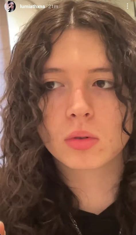 a close up of a person with long curly hair looking at the camera and holding a cell phone