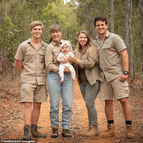 a group of people standing next to each other on a dirt road with trees ...