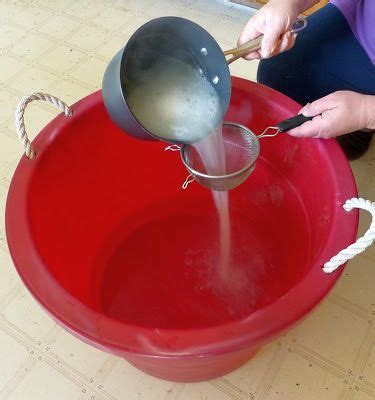 a woman is pouring water into a red bucket