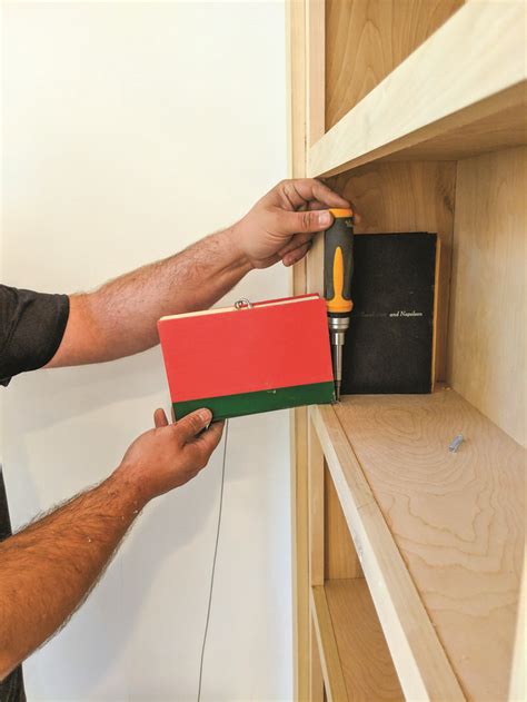 a man is holding a box with tools in it and he is working on the shelf