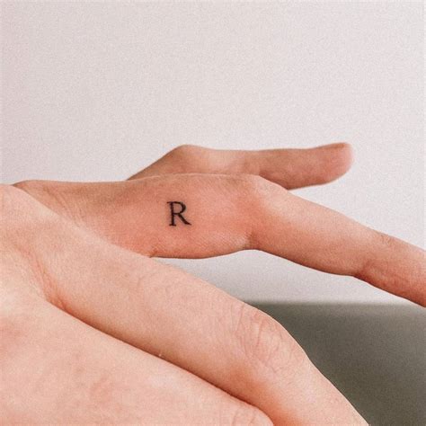 Minimalist letter "R" tattoo on the finger.