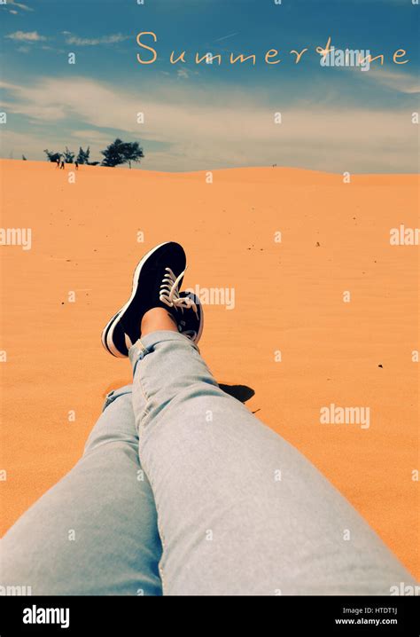 Summertime background with woman leg on sand hill, people relax on orange sandy under blue sky ...
