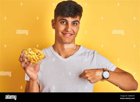 Young indian man holding bowl with dry pasta standing over isolated ...