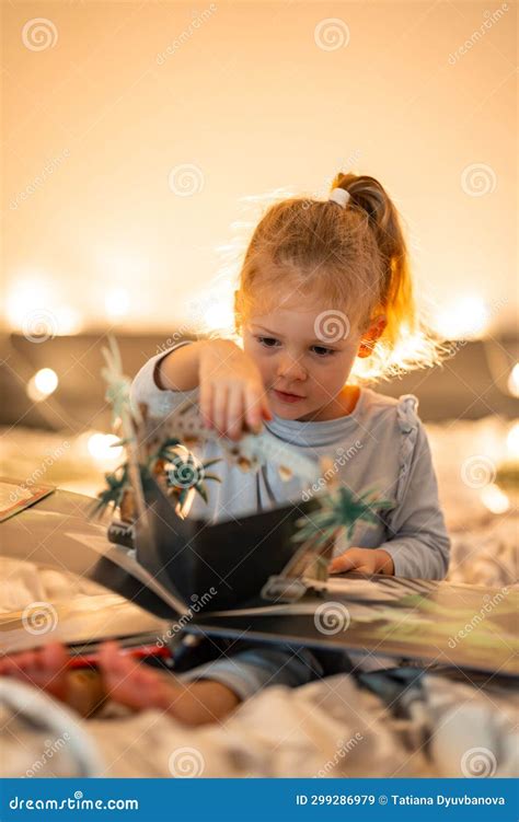 Little Girl Reading Pop Up Book in Home Bed in Christmas Environment with Lights Background ...