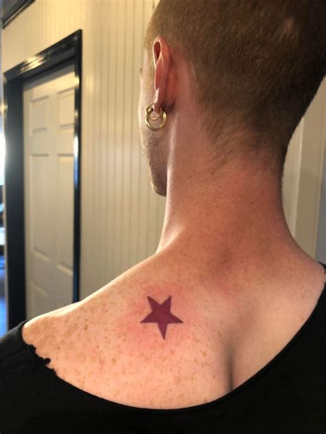 a man with a small star tattoo on his back shoulder and neck, standing in front of a door