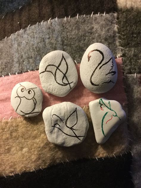 four rocks with faces drawn on them sitting on a blanket in front of a rug