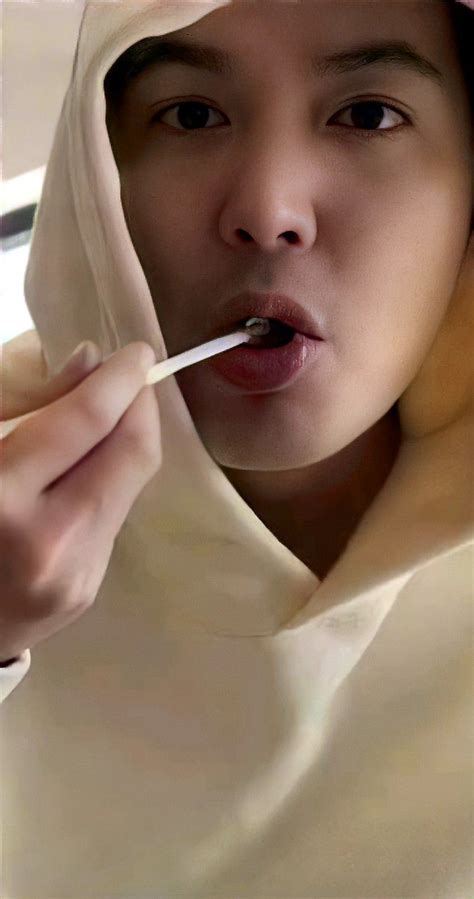 a woman brushing her teeth with a toothbrush in front of her face and wearing a white hood