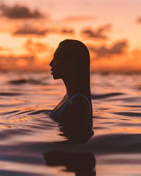 a woman in the water at sunset with her head turned to the side, looking off into the distance