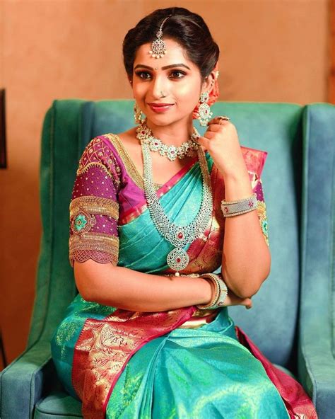 a woman in a green and pink sari sitting on a blue chair with jewelry