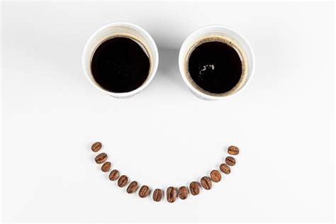 Smiling face - with coffee beans mouth and eyes from two paper cups of coffee. The concept of a ...