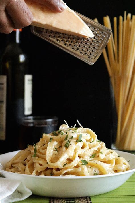 someone grating cheese on top of pasta in a white bowl