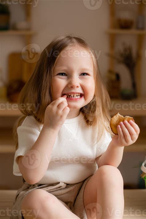 cute little girl eats natural pastille at home in a wooden kitchen. Food for children from ...