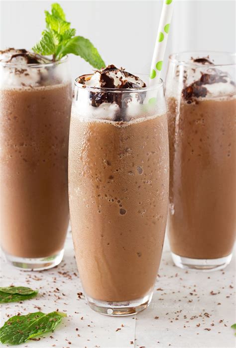 three glasses filled with chocolate milkshakes on top of a white table next to mint leaves