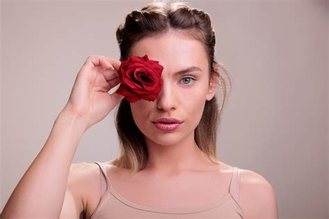 Premium Photo | Beautiful young woman covering eye with red rose bud ...