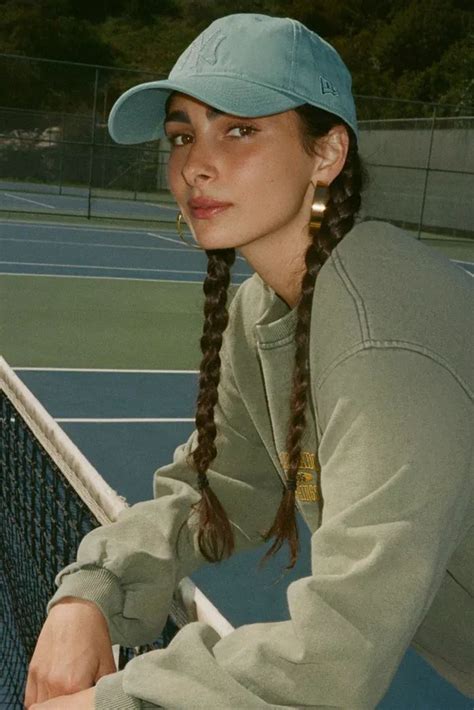 a woman with braids on her hair is leaning over a tennis court net and looking at the camera