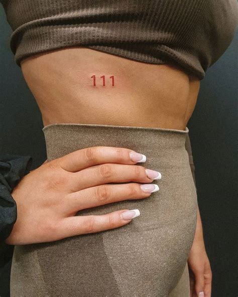 Angel number "111" tattooed on the rib, done in red