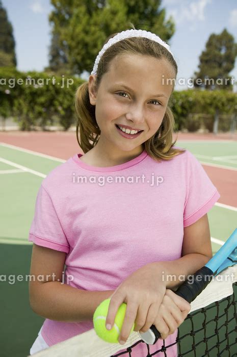 Young girl with tennis racket and ball by net at tennis court portraitの写真素材 [110704093] - イメージマート