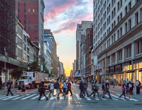 Crowds of people crossing an intersection in Manhattan, New York City with the colorful light of ...