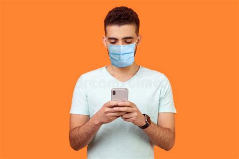 Portrait of Serious Man with Medical Mask in Casual White T-shirt Using Cellphone, Texting ...