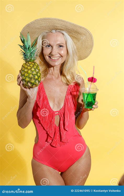 Joyful Blonde Woman in Red Swimsuit and Straw Hat Smiling at Camera, Holding Fresh Pineapple ...