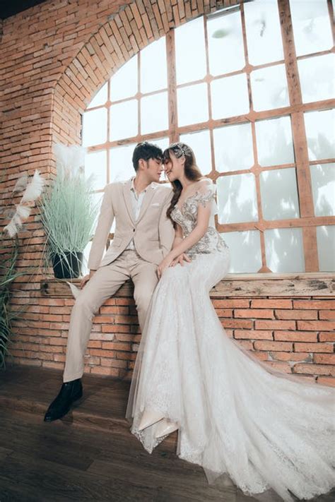 Delighted Asian newlywed couple cuddling while resting on windowsill · Free Stock Photo