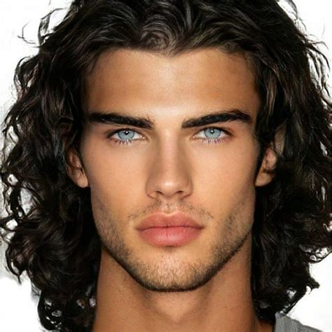 a man with long hair and blue eyes looks at the camera while wearing a gray shirt