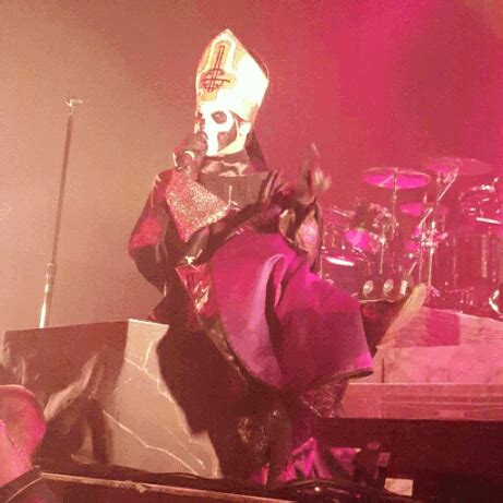 a man with a mask on standing in front of a drum set at a concert