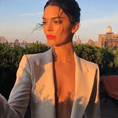a woman wearing a white suit and red lipstick standing in front of a cityscape