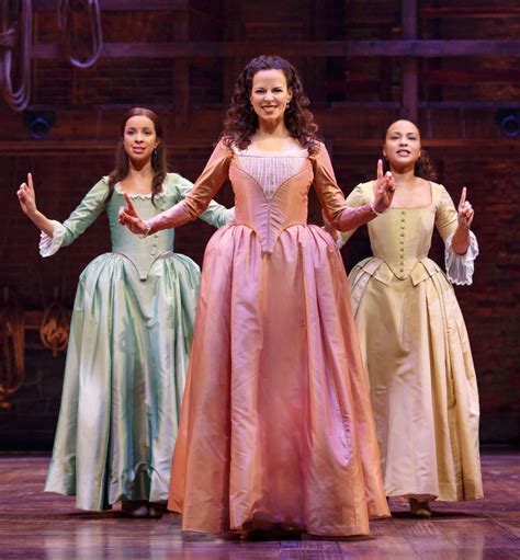 three women in dresses standing on stage with their hands up and one woman holding her arms out