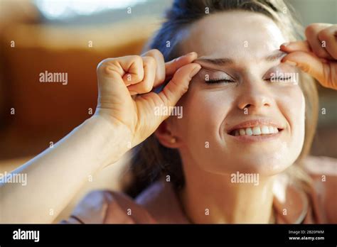 happy elegant housewife in pajamas at modern home in sunny winter day making facial massage ...