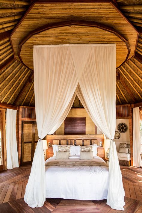 a bed with white drapes on top of it in a room filled with wooden floors