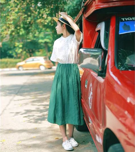 a woman leaning against the side of a red truck wearing a hat and green skirt