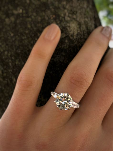 a woman's hand with a diamond ring on top of her finger, next to a rock