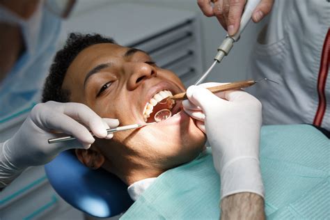 cleanings Dentist examining oral cavity of young African-American man working in in dental ...