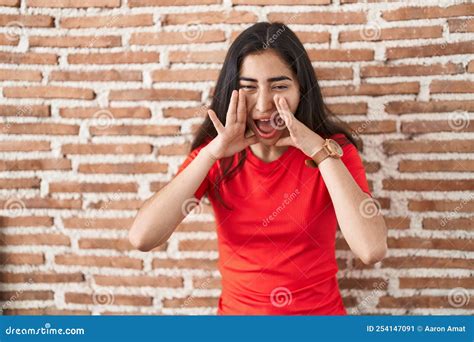 Young Teenager Girl Standing Over Bricks Wall Shouting Angry Out Loud with Hands Over Mouth ...