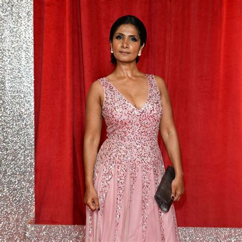 a woman standing in front of a red curtain wearing a pink dress and holding a black purse