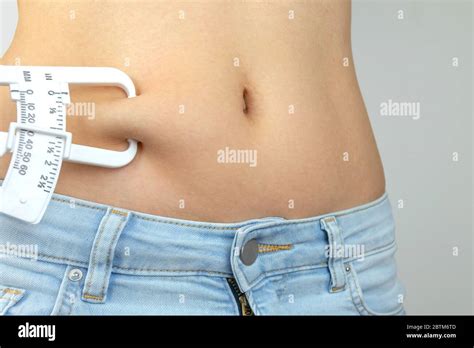 Body fat calipers, woman measuring subcutaneous percentage of fat on her belly. Young woman ...