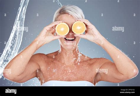 Water splash, fruit and senior skincare of a woman holding orange for vitamin c and skin glow ...
